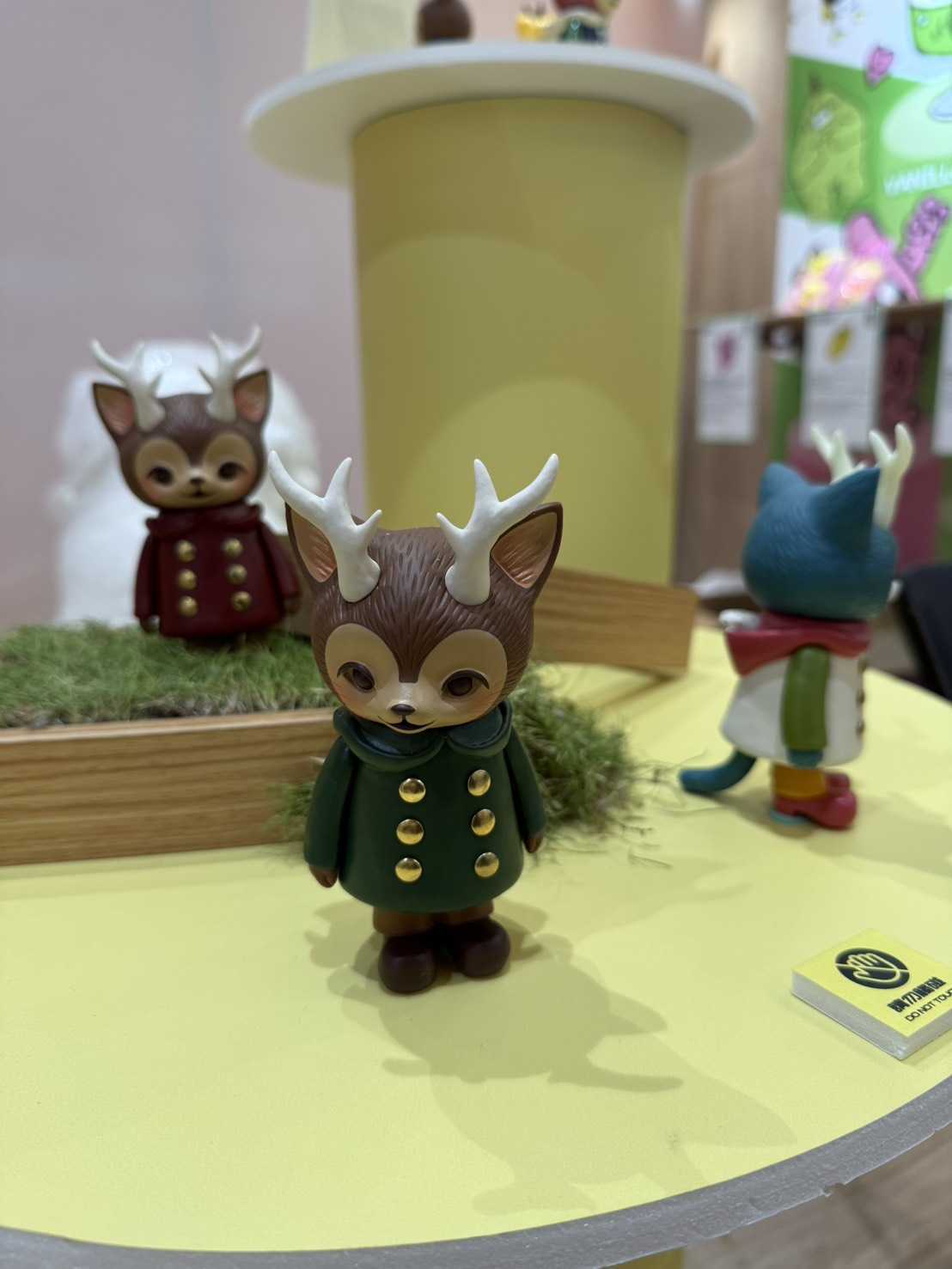 MORRIS, The Cat with Antlers figures dressed in coats, displayed on a moss bed at Winter Fantasy