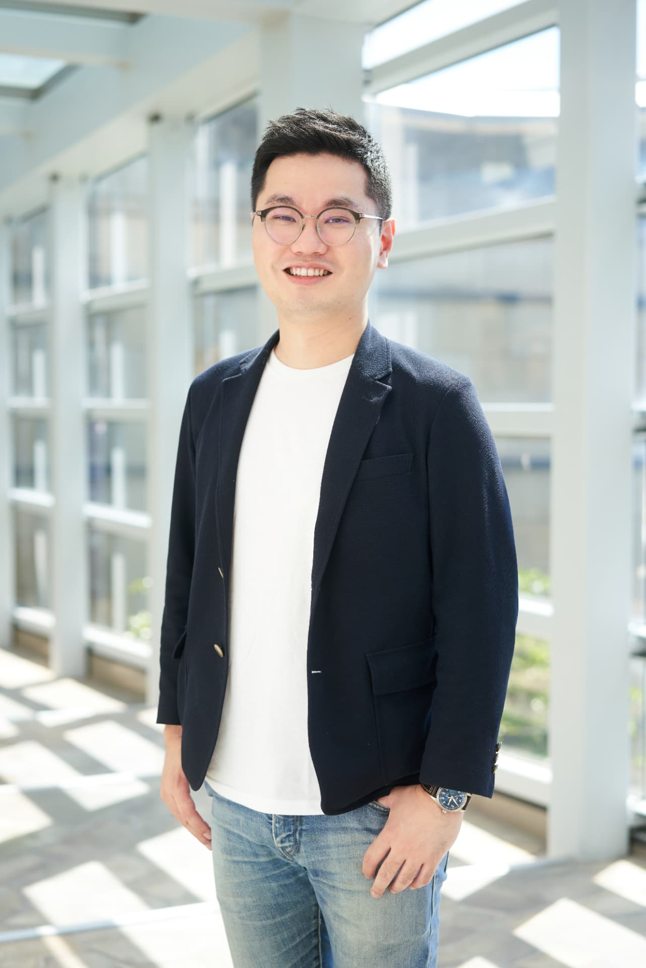 Portrait of Wilson Tai standing in front of a bright windowed facade