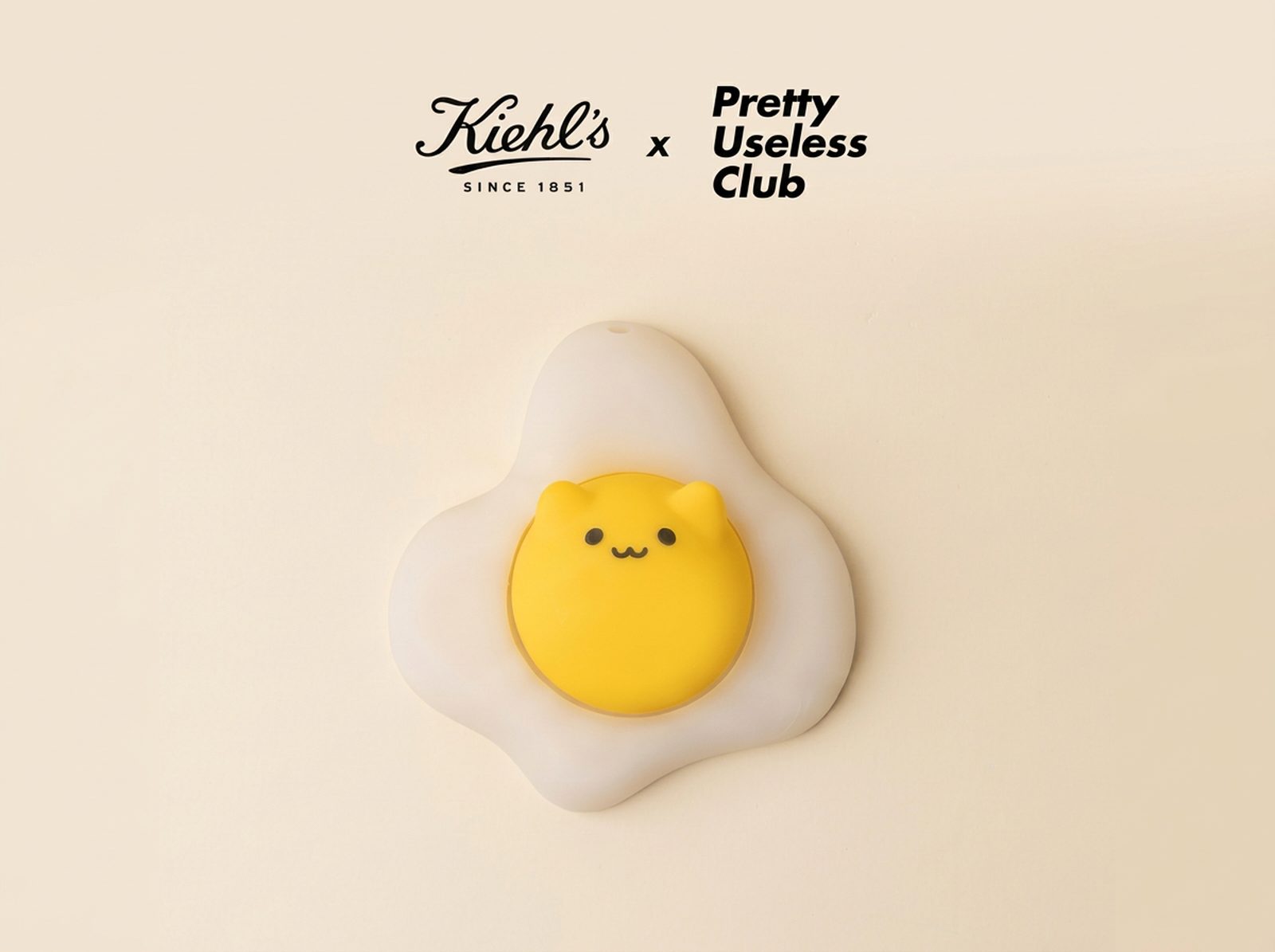 A Kiehl’s x Pretty Useless Club Sunny Egg clicker shaped like a fried egg with a smiling yellow yolk, photographed on a cream background
