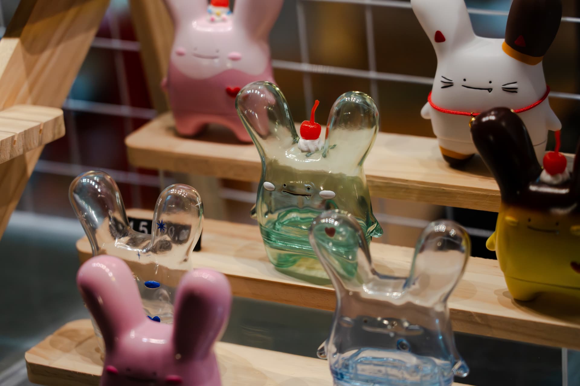 Rabitt Planet bunny figures arranged on tiered wooden display shelves at the Midnight Walk night market, led by a translucent green figure topped with whipped cream and a cherry